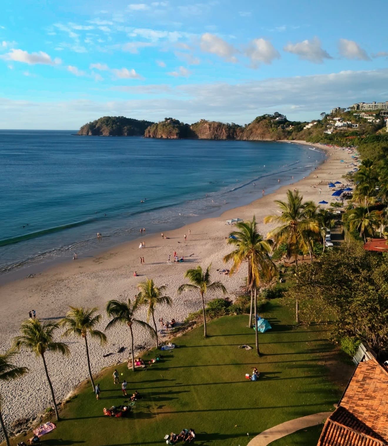 Aerial view of Playa Flamingo in Costa Rica showing the crescent bay, pale sand, two rocky headlands, turquoise Pacific water, and the hillside villas above the beach
