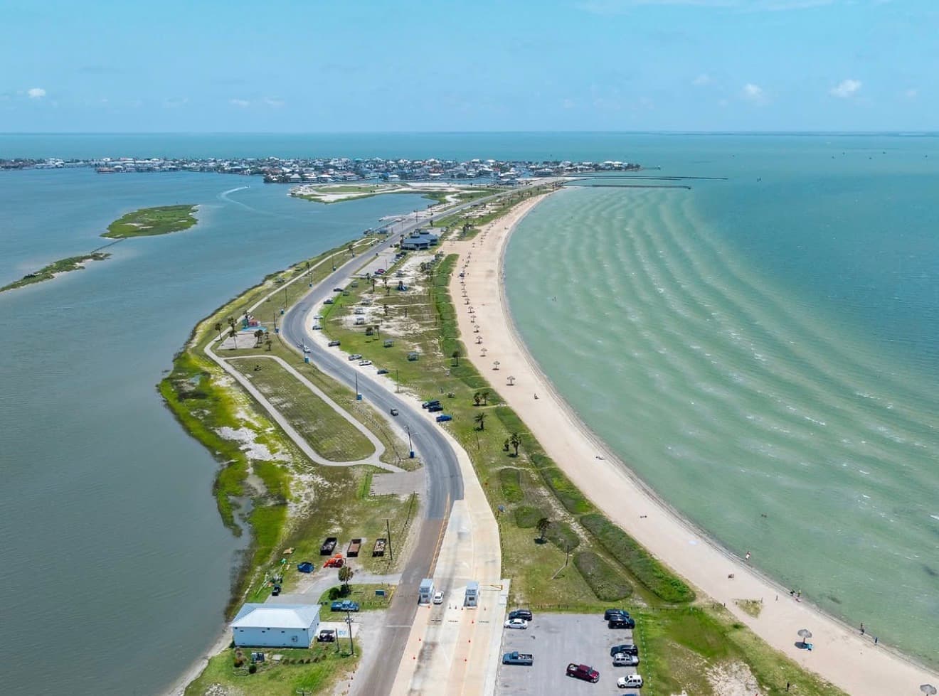 Aerial view of Rockport Beach Park in Texas showing the curved bay beach, palapas along the sand, Little Bay inlet, and parking area on a clear day
