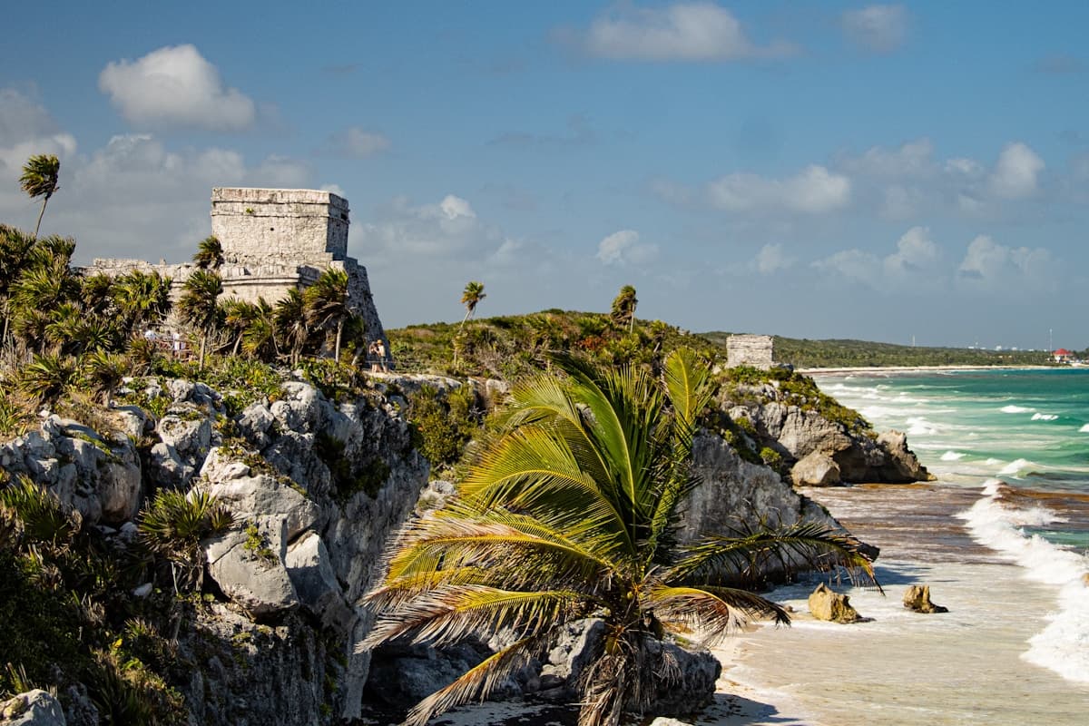 Turquoise Caribbean water and white sand at Tulum Beach with the Mayan ruins visible on the clifftop above