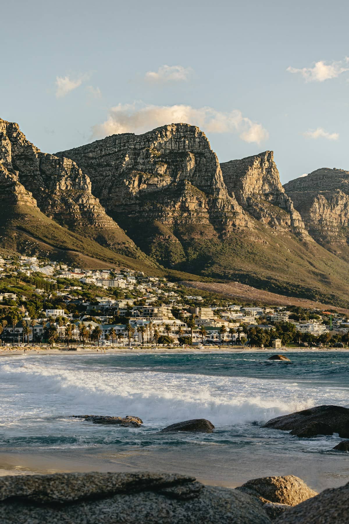 White sand beach at Camps Bay with the Twelve Apostles mountain range rising behind palm trees and turquoise Atlantic water