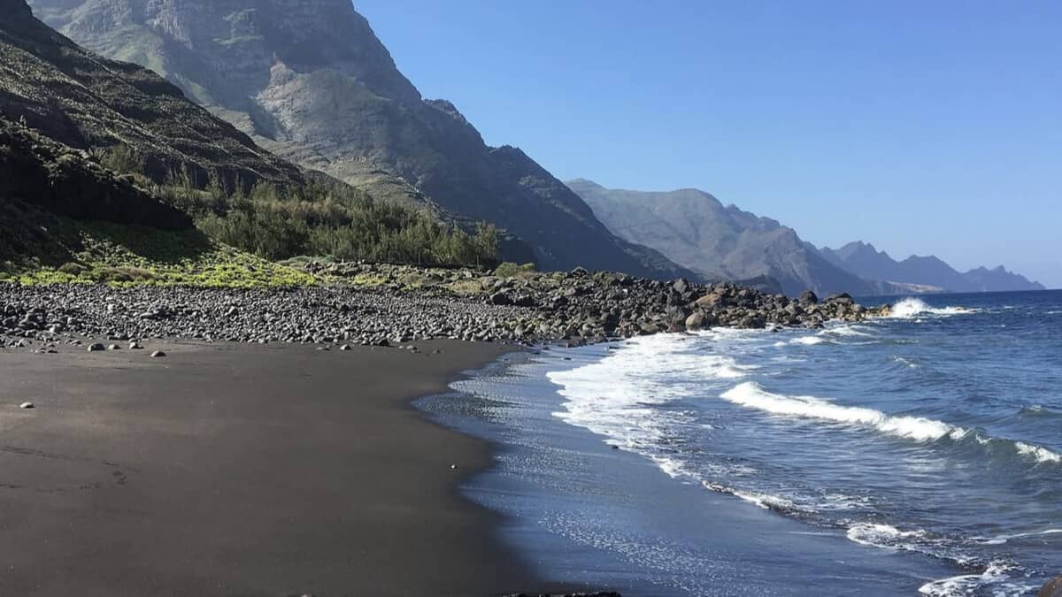 The black volcanic sand and boulder shore of Playa de Guayedra beneath the cliffs of the Tamadaba massif on Gran Canaria