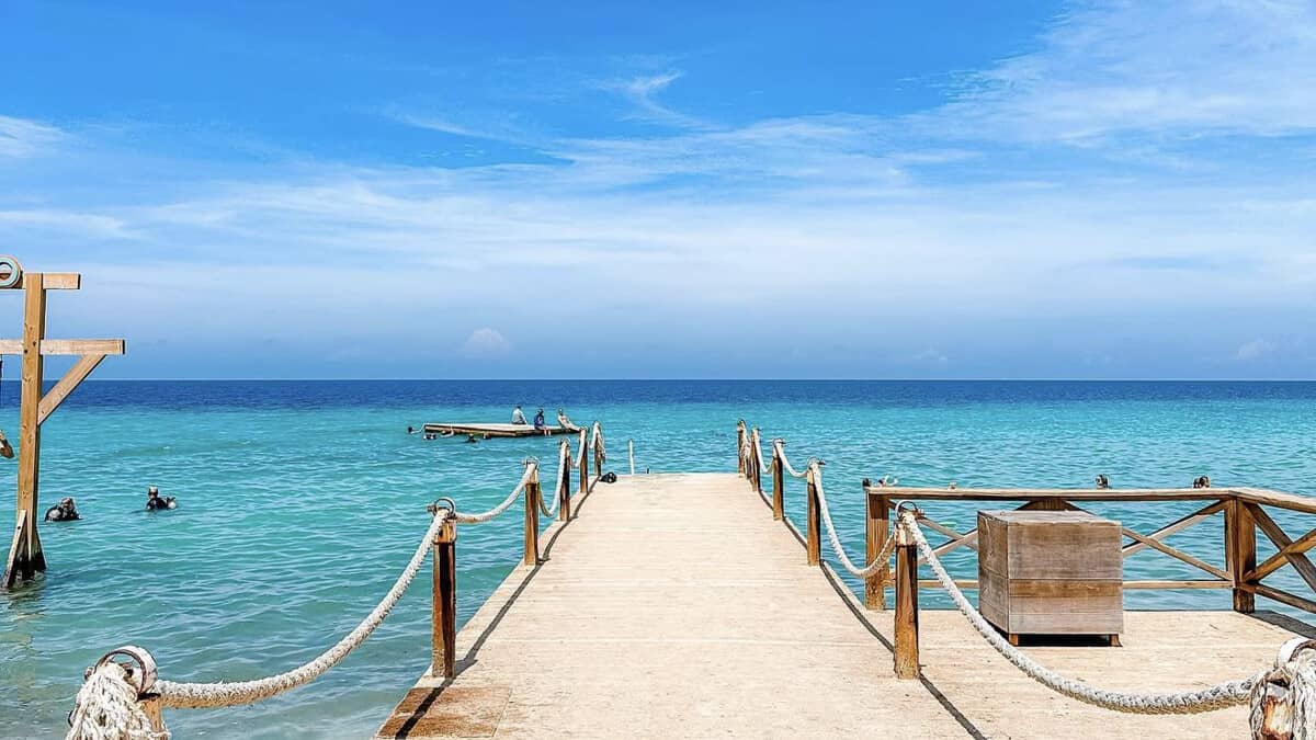 The wooden jetty at Kokomo Beach in Curacao, with rope railings leading out over clear turquoise water to a swimming platform, with snorkellers in the bay