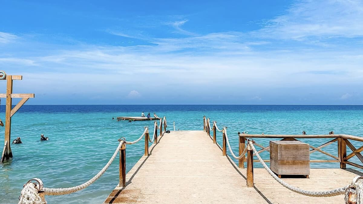 The wooden jetty at Kokomo Beach in Curacao, with rope railings leading out over clear turquoise water to a swimming platform, with snorkellers in the bay
