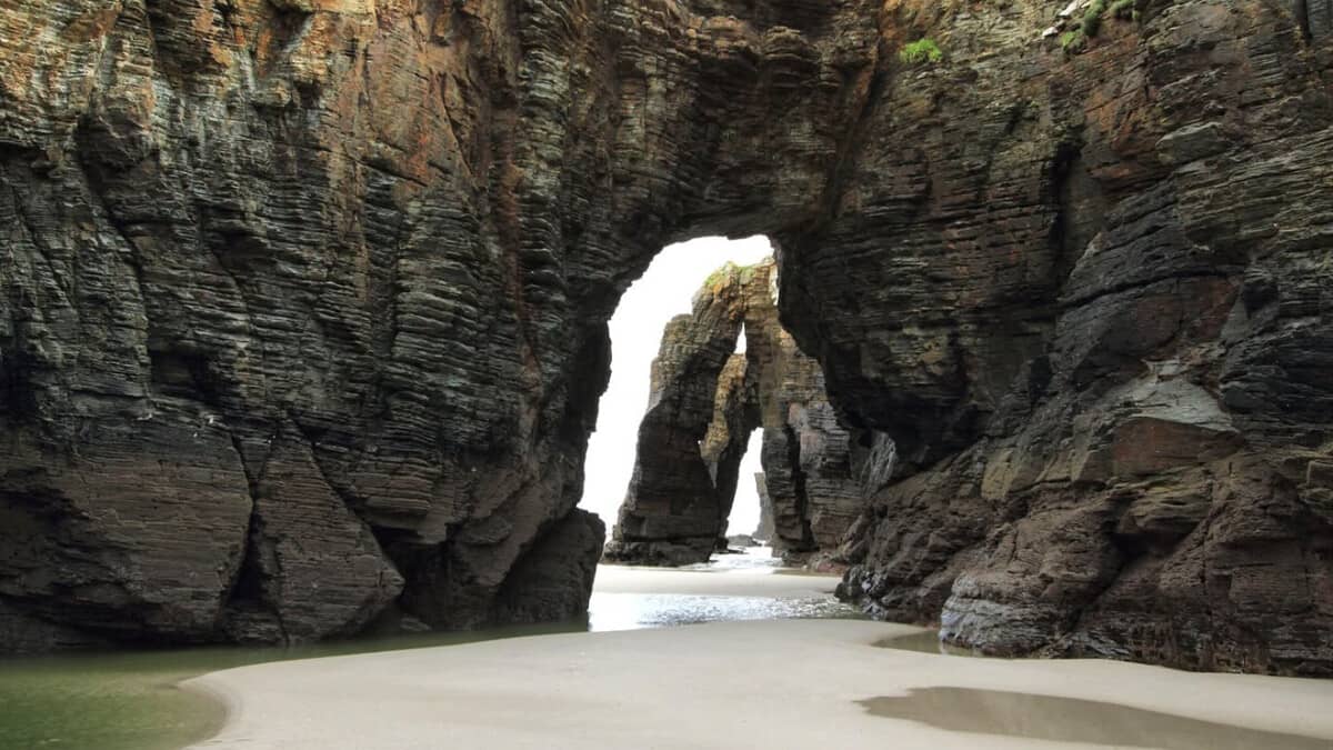 The great stone arches of Praia das Catedrais at low tide, their buttresses rising from the wet sand on the Galician coast