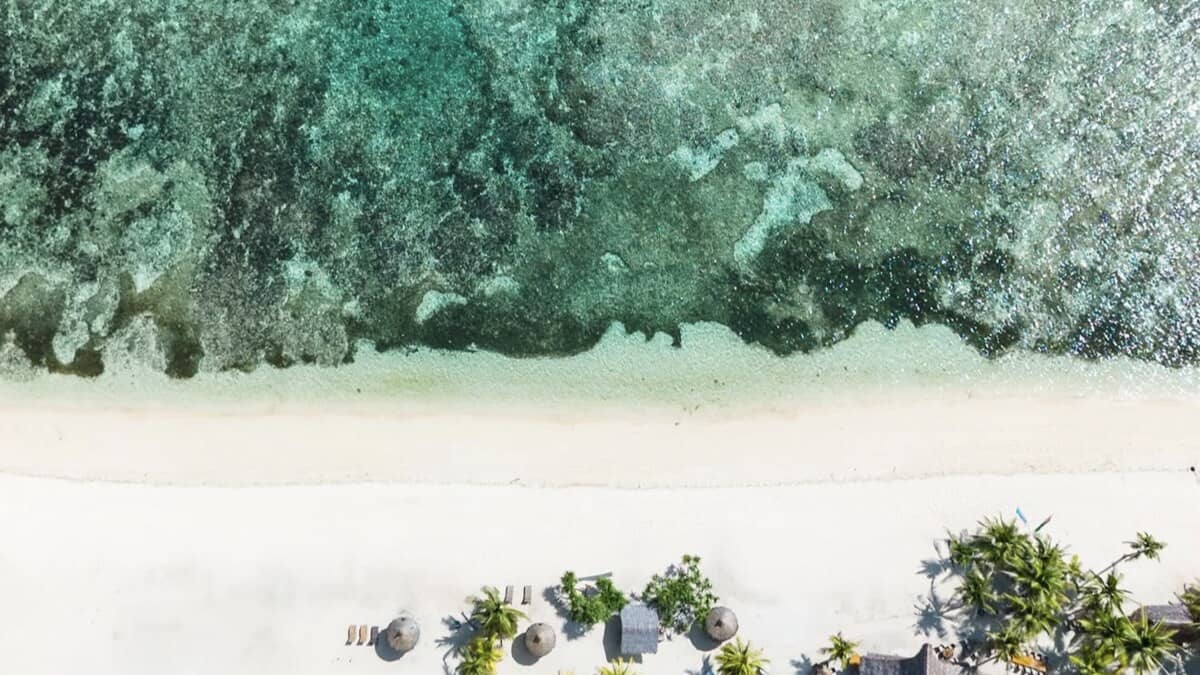 Aerial of Tubod Beach on Siquijor, white sand and palm-shaded cabanas meeting clear turquoise water over the protected reef just offshore