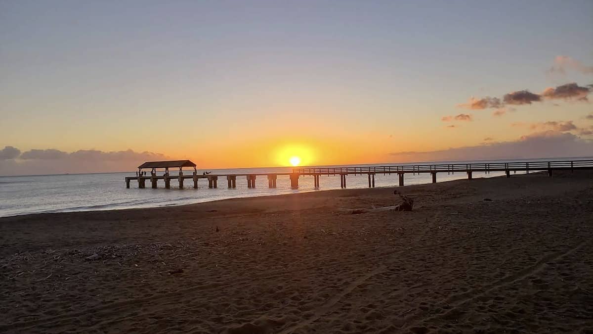 Waimea Beach Kauai with the historic state pier extending into the river-mouth bay and dark sand