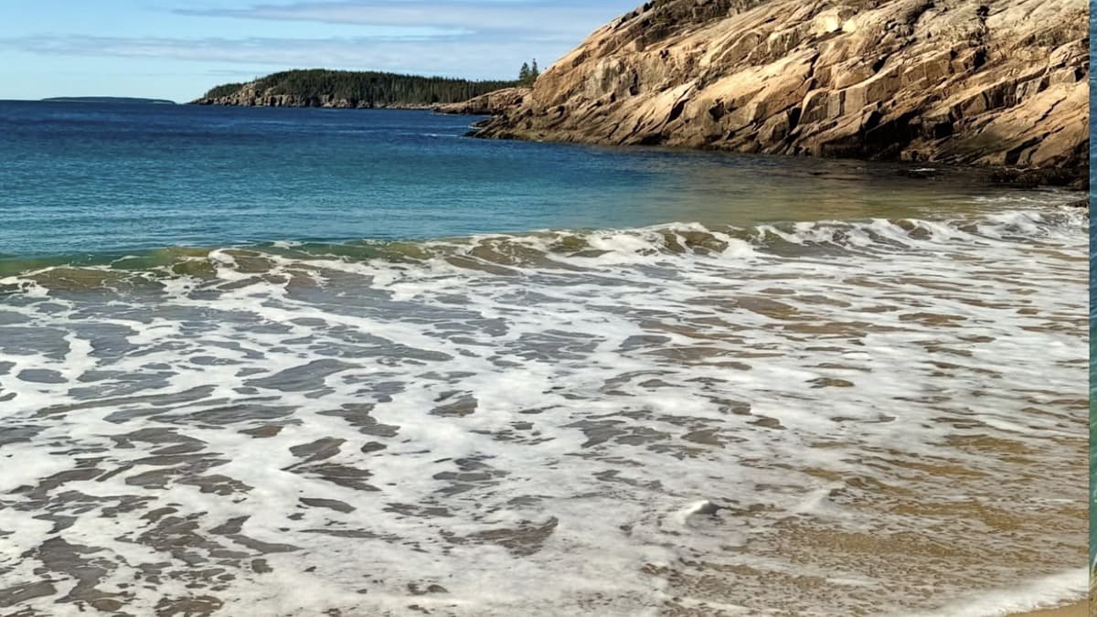 Pink-tinged sand at Sand Beach in Acadia National Park enclosed by granite cliffs