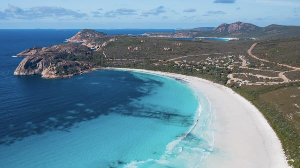 Aerial view of Lucky Bay's white sand crescent meeting turquoise water at Cape Le Grand National Park near Esperance, with the campground and granite headland behind