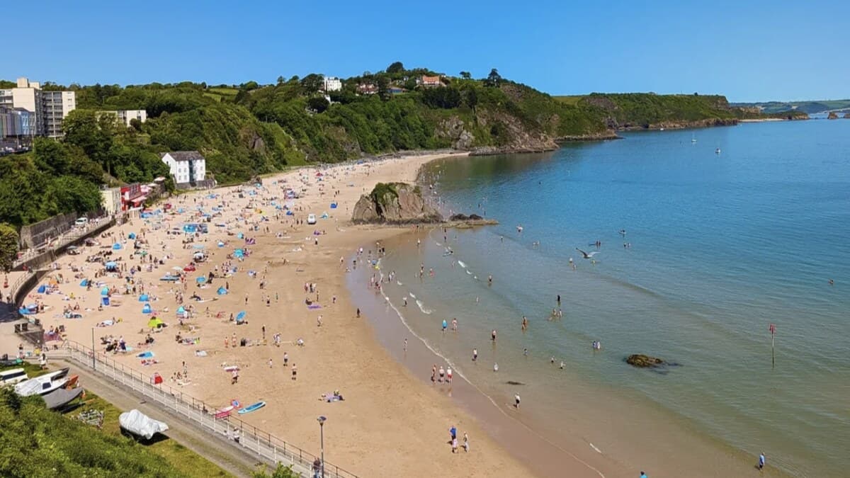 Tenby North Beach in Pembrokeshire on a busy summer day, families on the golden sand around Goscar Rock below the town's green headland