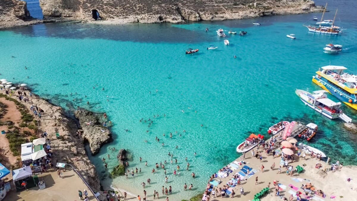The Blue Lagoon at Comino in Malta packed with tour boats and swimmers in peak summer, its turquoise water crowded with day-trippers