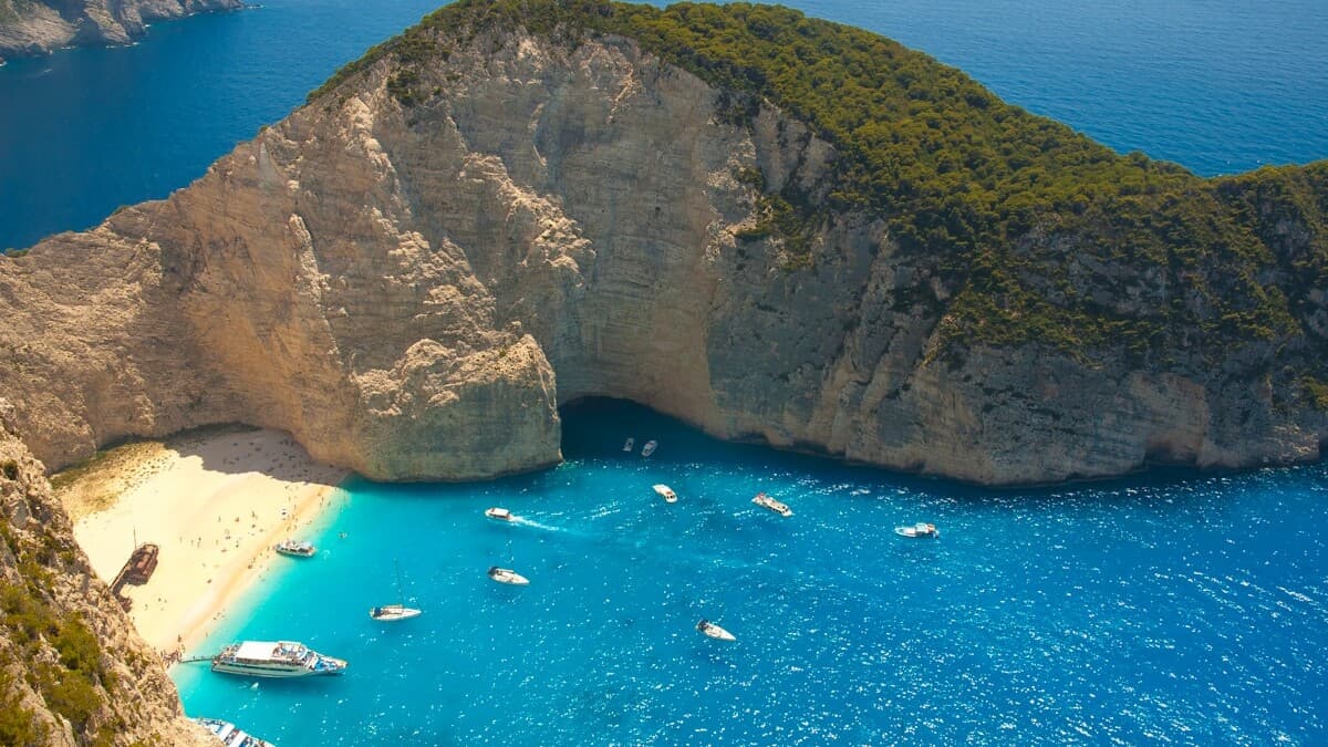The turquoise water and white-sand cove of Navagio Shipwreck Beach on Zakynthos, framed by tall limestone cliffs, in the Ionian islands of Greece