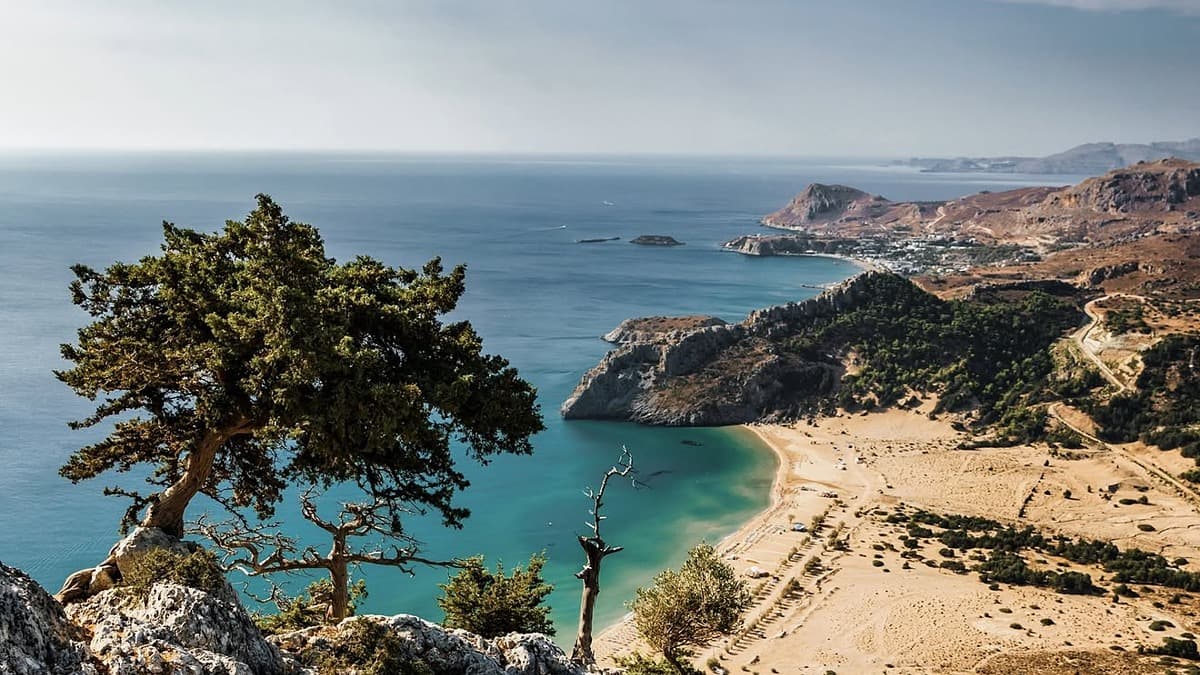 Tsampika beach on Rhodes, wide golden sand and shallow turquoise water below the monastery hill, still in full summer conditions
