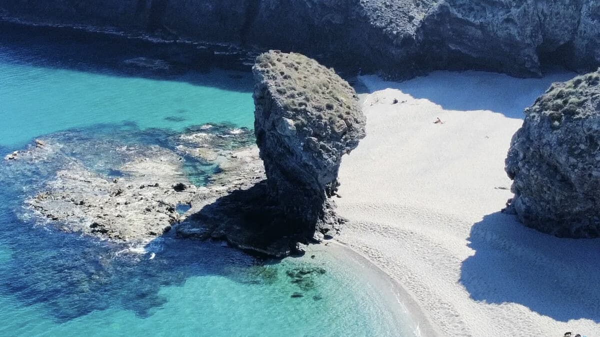 Playa de los Muertos in Cabo de Gata, white pebbles and clear turquoise water around a rock stack beneath dark cliffs, almost empty