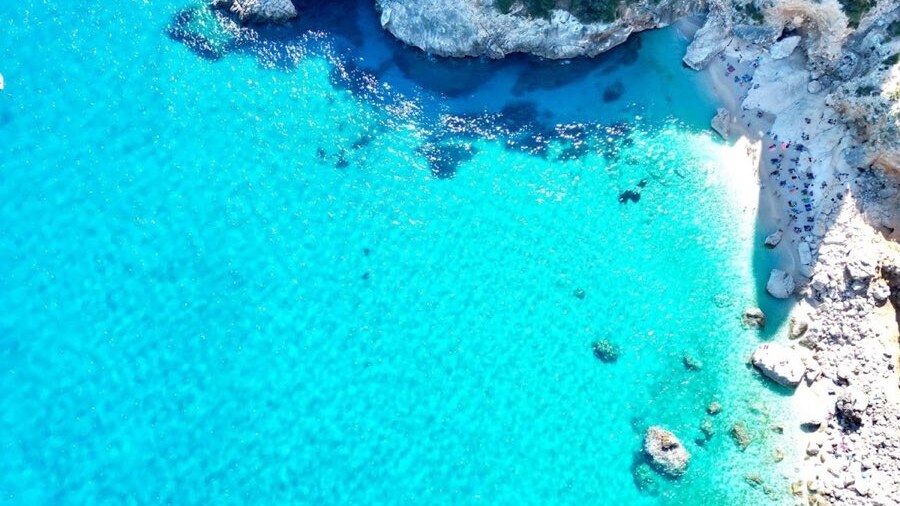 Aerial view of Cala Goloritze in Sardinia, turquoise water and a white pebble beach below pale limestone cliffs