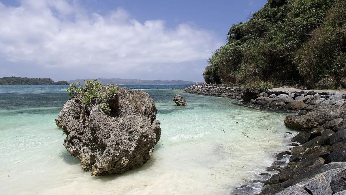 Ilig-Iligan Beach on Boracay, a large weathered rock standing in clear shallow water beside a rocky shore and forested headland