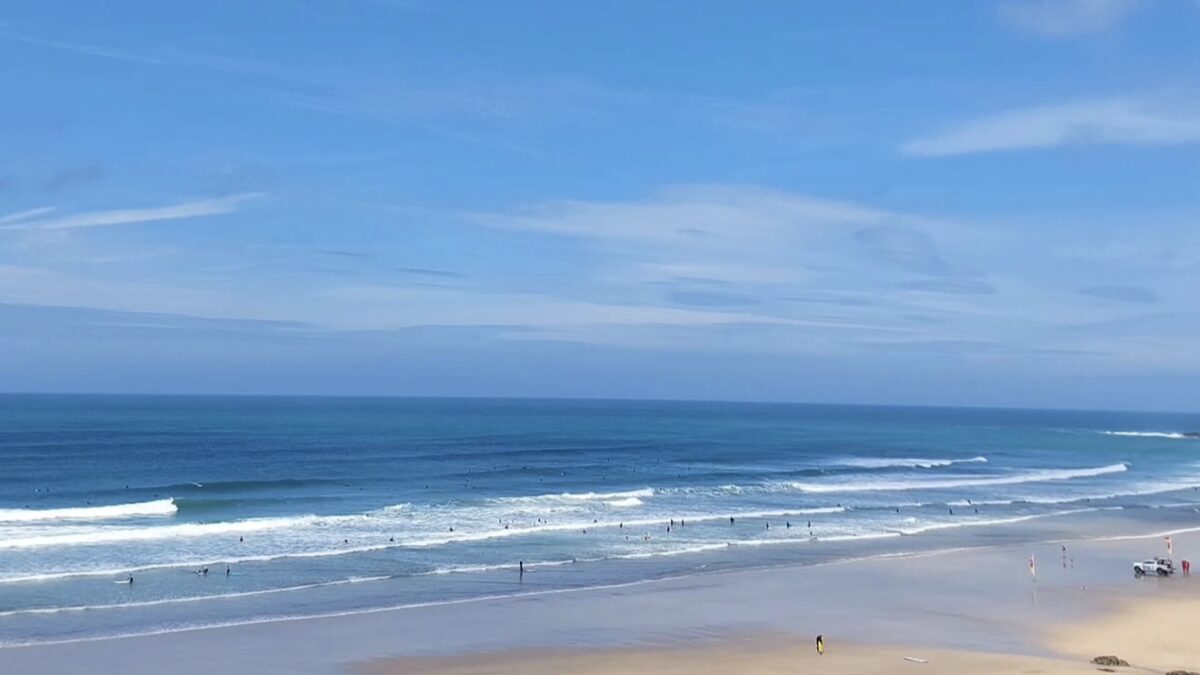 Fistral Beach Newquay with lines of Atlantic surf rolling in, surfers in the water and lifeguard flags on the wide sand