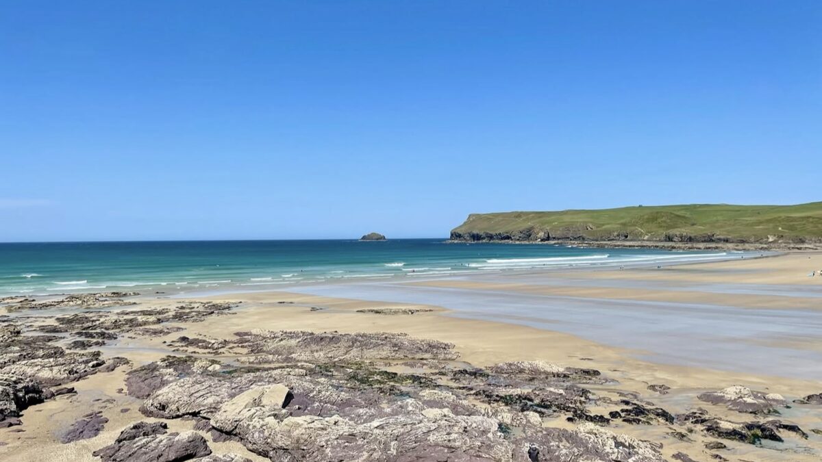 Polzeath Beach, wide golden sands at low tide with rock ledges and the green headland in north Cornwall
