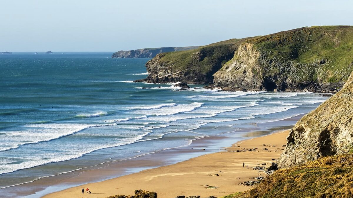 Watergate Bay's long wide beach backed by tall dark cliffs north of Newquay, with surfers and walkers on the sand