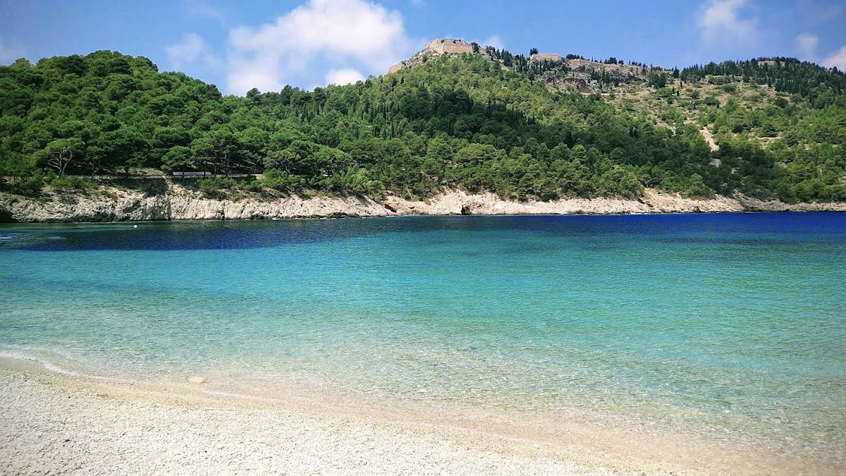 A clear turquoise pebble cove backed by a forested headland on the Assos peninsula, Kefalonia