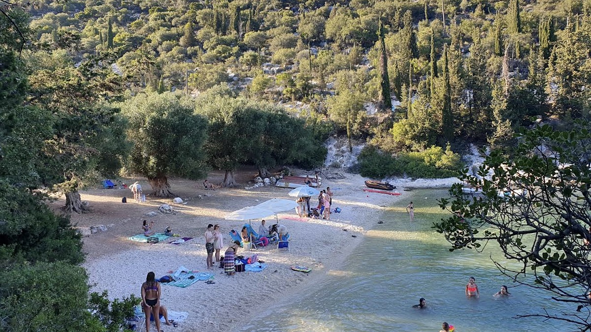 Foki Beach near Fiskardo, a small pebble cove shaded by pine and cypress trees with clear calm water