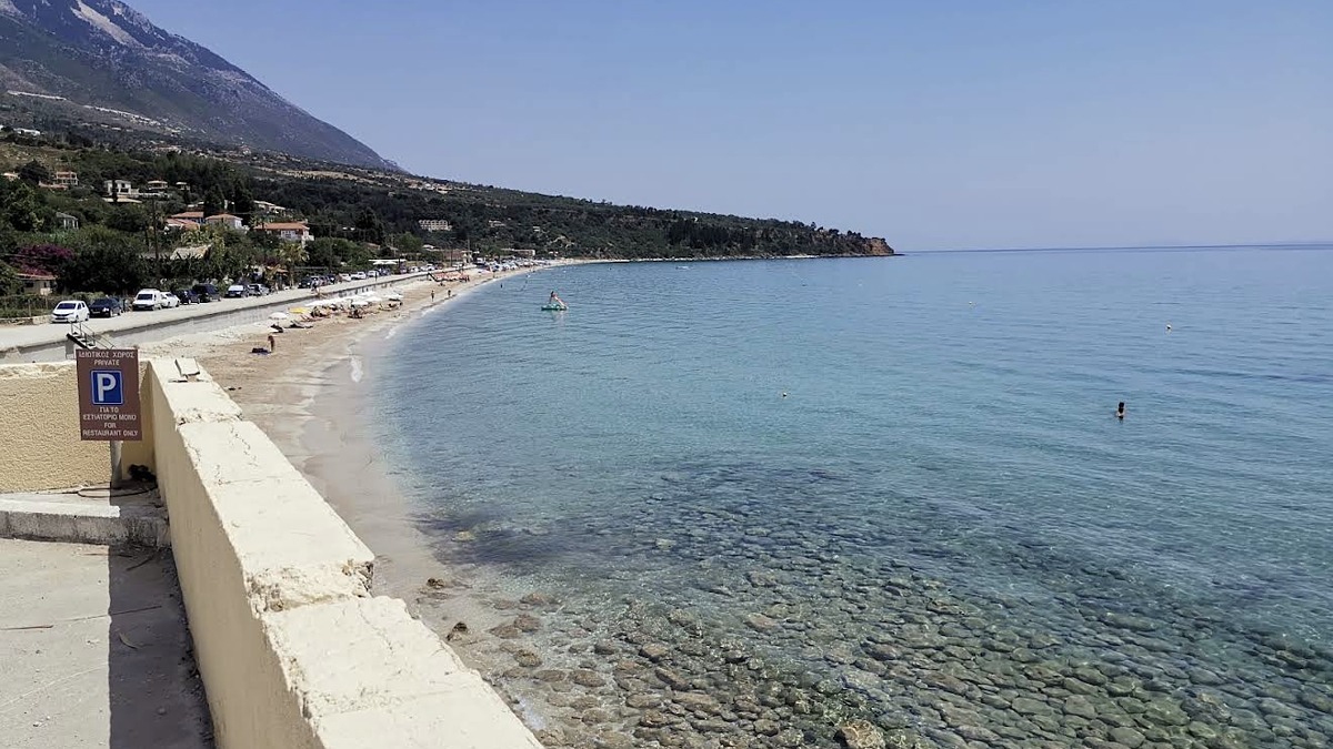 Lourdas Beach on the south coast with shallow water, organised loungers and a row of beachfront tavernas