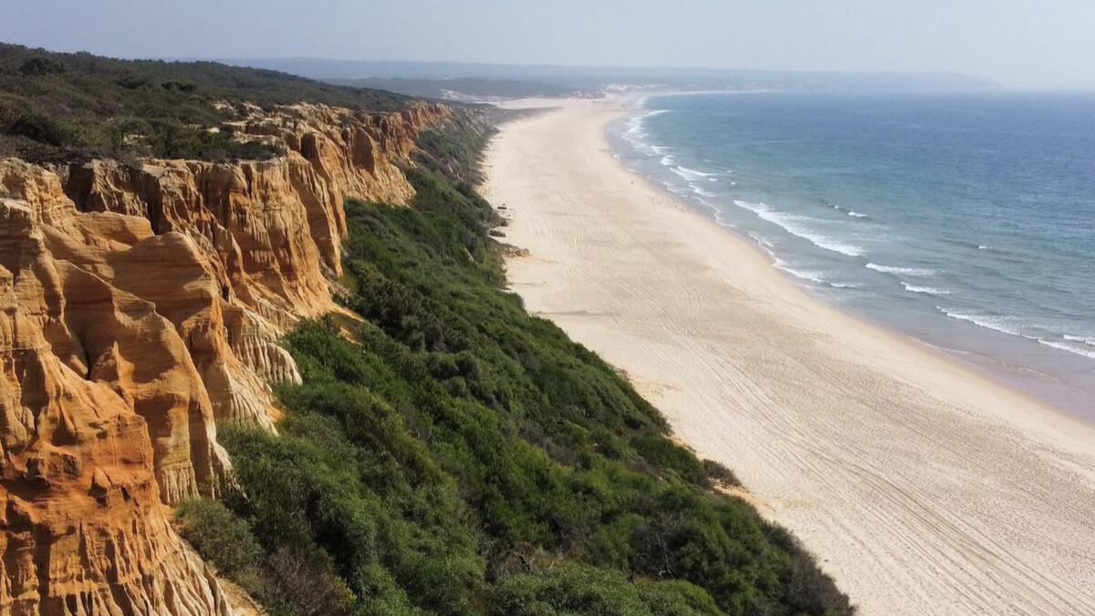 Costa da Caparica's seemingly endless flat sand backed by low dunes and fossil cliffs under a wide-open Atlantic sky