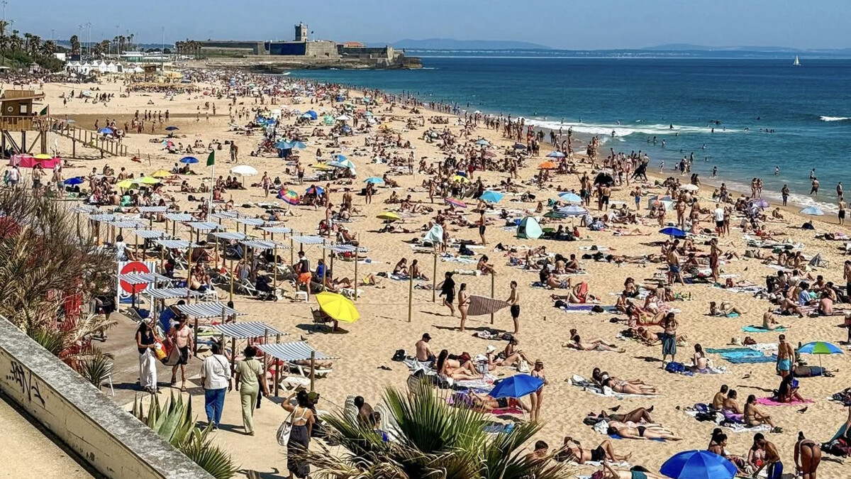 The long wide sweep of Carcavelos beach with surfers and the Sao Juliao fort at the far end