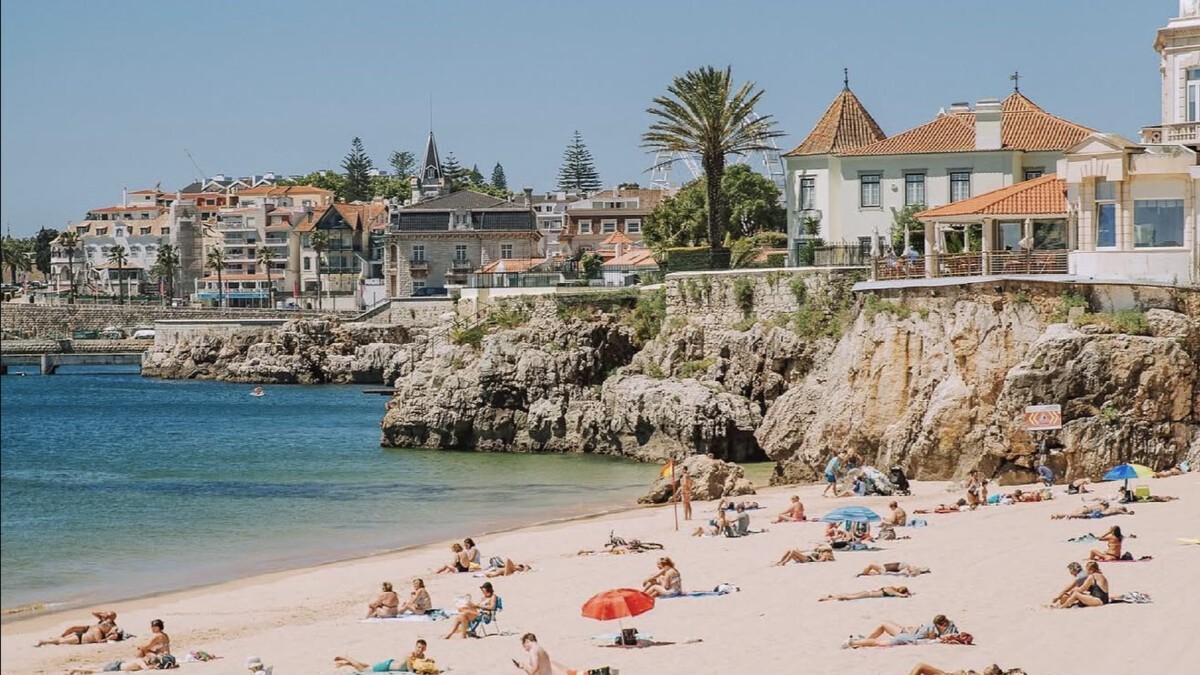 Praia da Conceicao in Cascais, a sheltered arc of golden sand with sunbathers, the bay and the town promenade behind