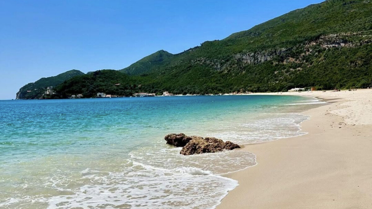 Portinho da Arrabida cove with white buildings on the shore, calm clear water and the bright-blue bay sheltered by green cliffs