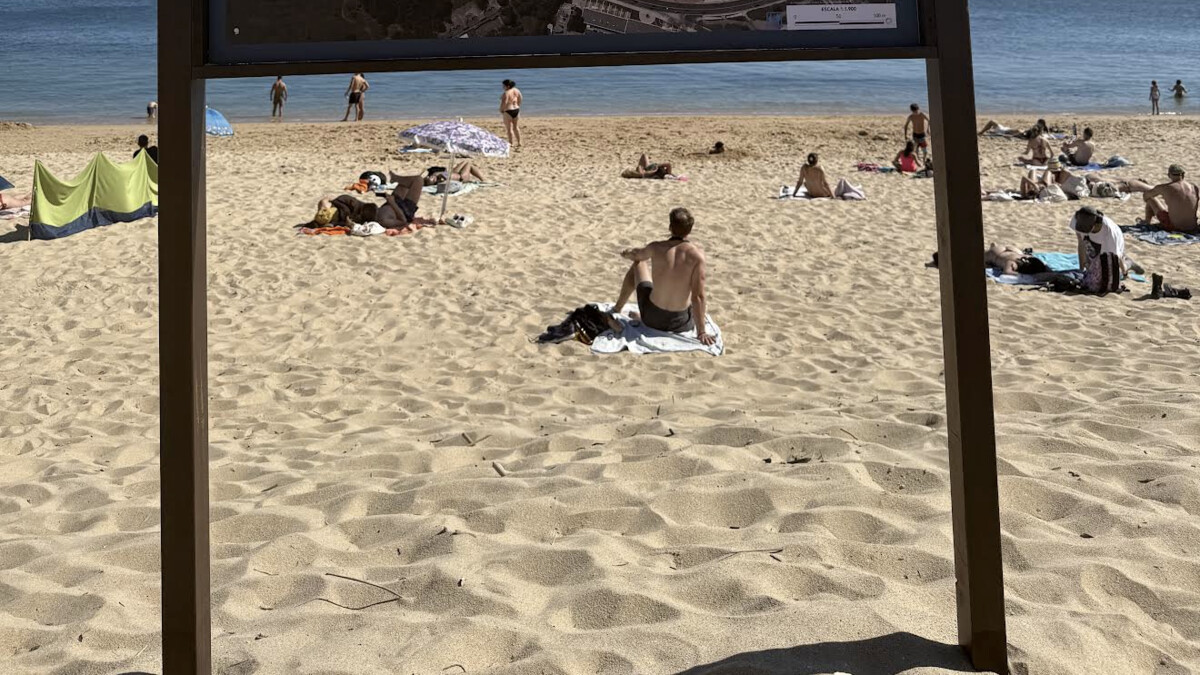 Praia de Santo Amaro de Oeiras near Lisbon, sunbathers on the sand and calm Tagus-mouth water seen past the beach's Blue Flag information board