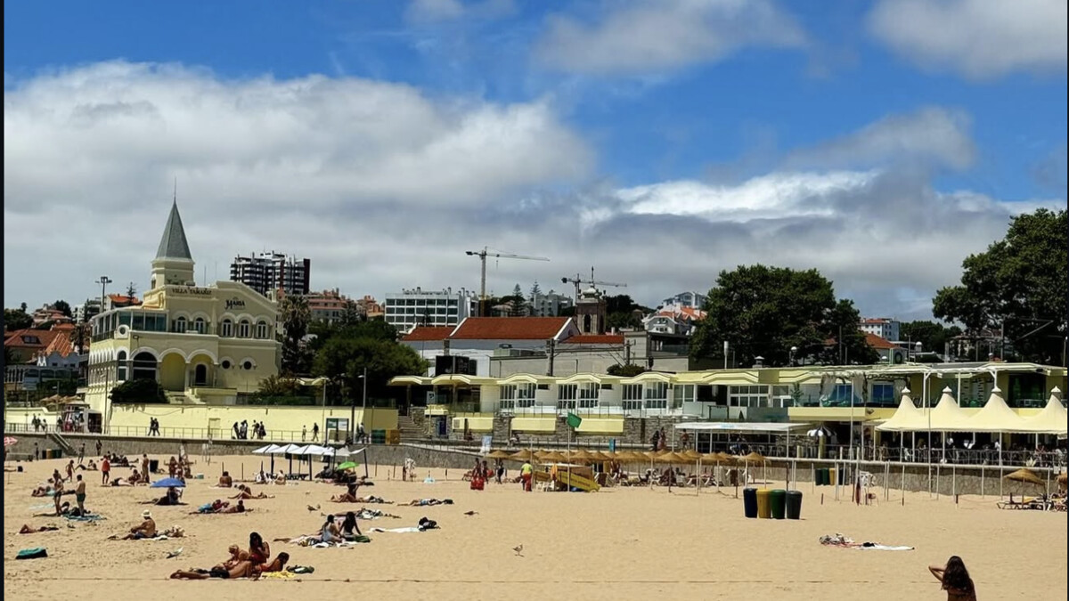Praia do Tamariz in Estoril, the busy town beach with the seafront promenade buildings and pavilion behind the sand
