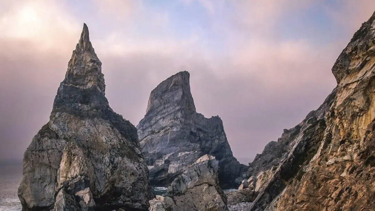 Praia da Ursa's dramatic sea stacks, including the needle-like pinnacle, rising from the Atlantic below the Sintra cliffs at dusk