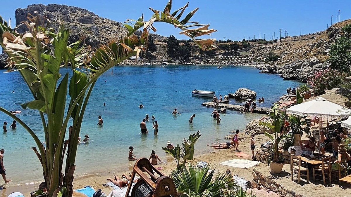 Lindos beach below the ancient acropolis on its headland, with sandy shore and calm protected water on Rhodes