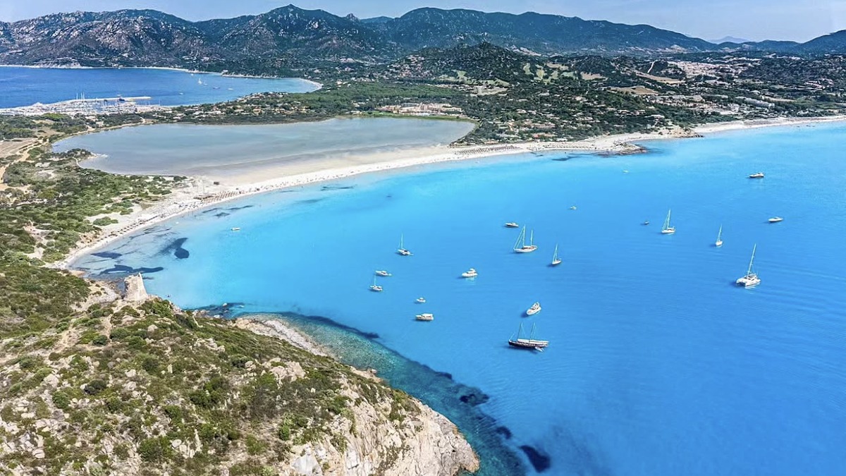 Porto Giunco in southeast Sardinia, a long white-sand beach between rocky headlands with a flamingo lagoon behind