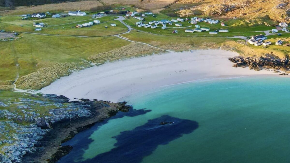 Achmelvich's small sheltered white-sand cove with shallow clear turquoise water and a rocky headland backdrop near Lochinver