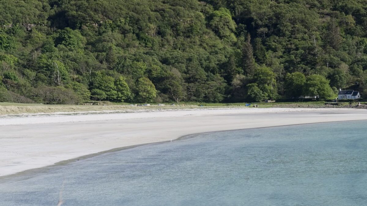 Calgary Bay on the Isle of Mull, a sheltered white-sand bay with clear turquoise water backed by green woodland and a white cottage