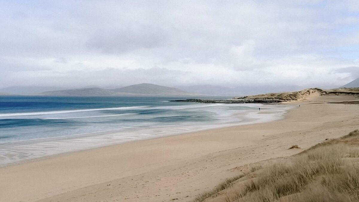 Scarista beach on west Harris, golden-white sand sweeping below the road with surf rolling in, more windswept than Luskentyre