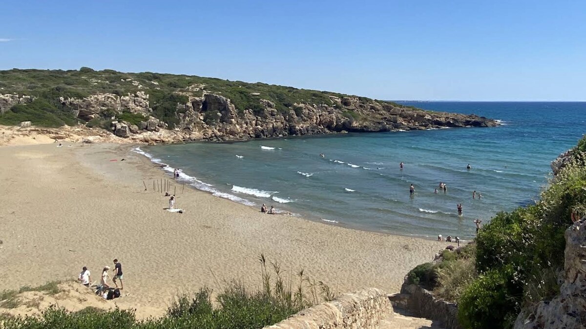 Calamosche in the Vendicari reserve, a sheltered sandy inlet between rocky headlands with clear shallow water, a few swimmers and no buildings