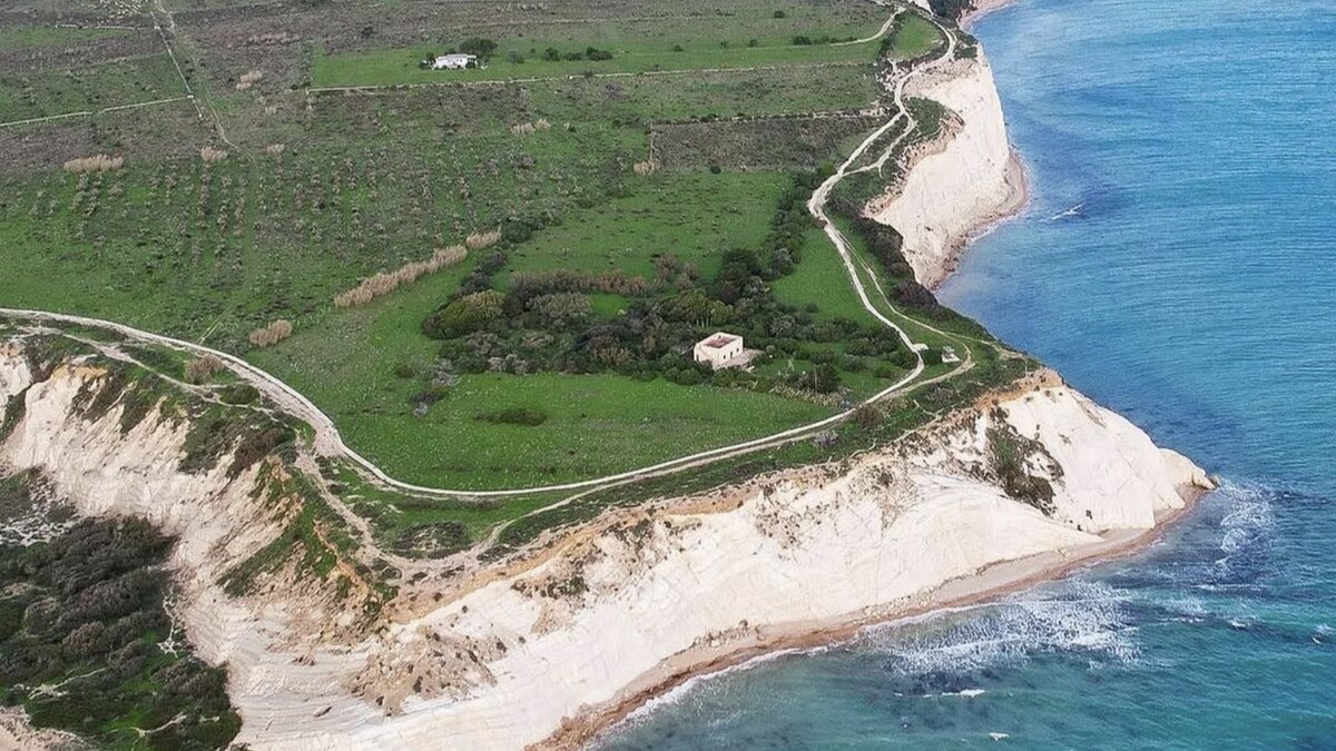 Aerial of Eraclea Minoa in southern Sicily, pale marl cliffs and a green headland of farmland and scrub dropping to a quiet beach and the open sea