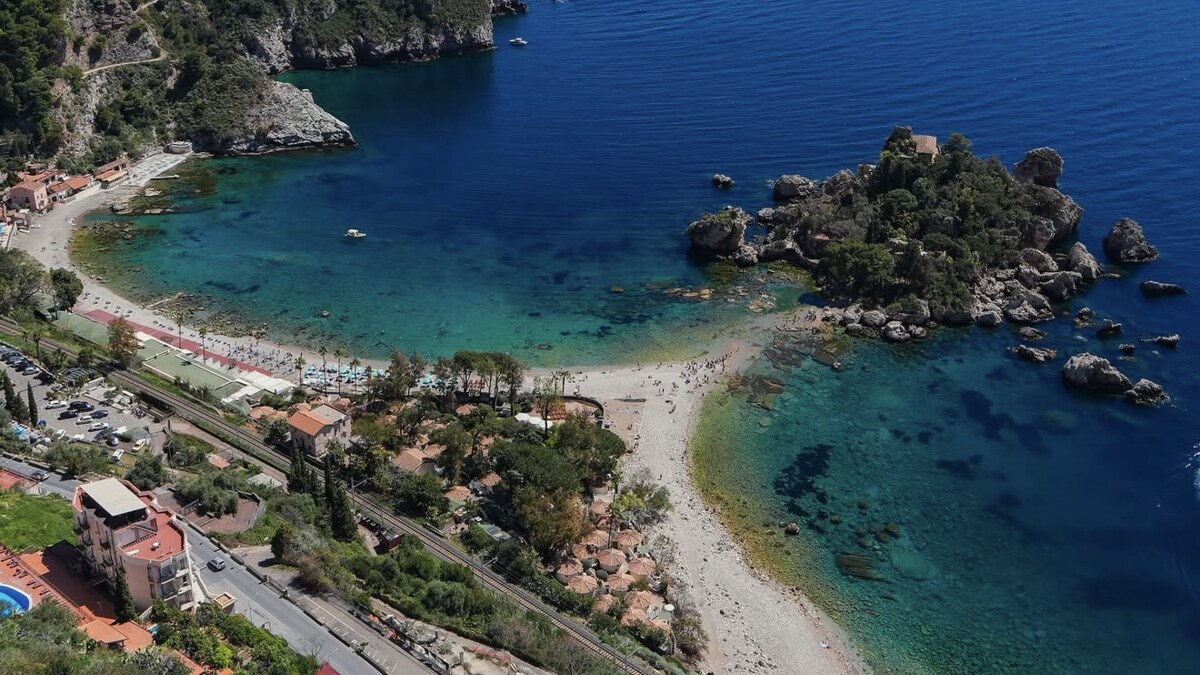 Isola Bella below Taormina, the tiny green islet joined to the shore by a thin pebble spit between two clear turquoise bays, seen from the cliffs above