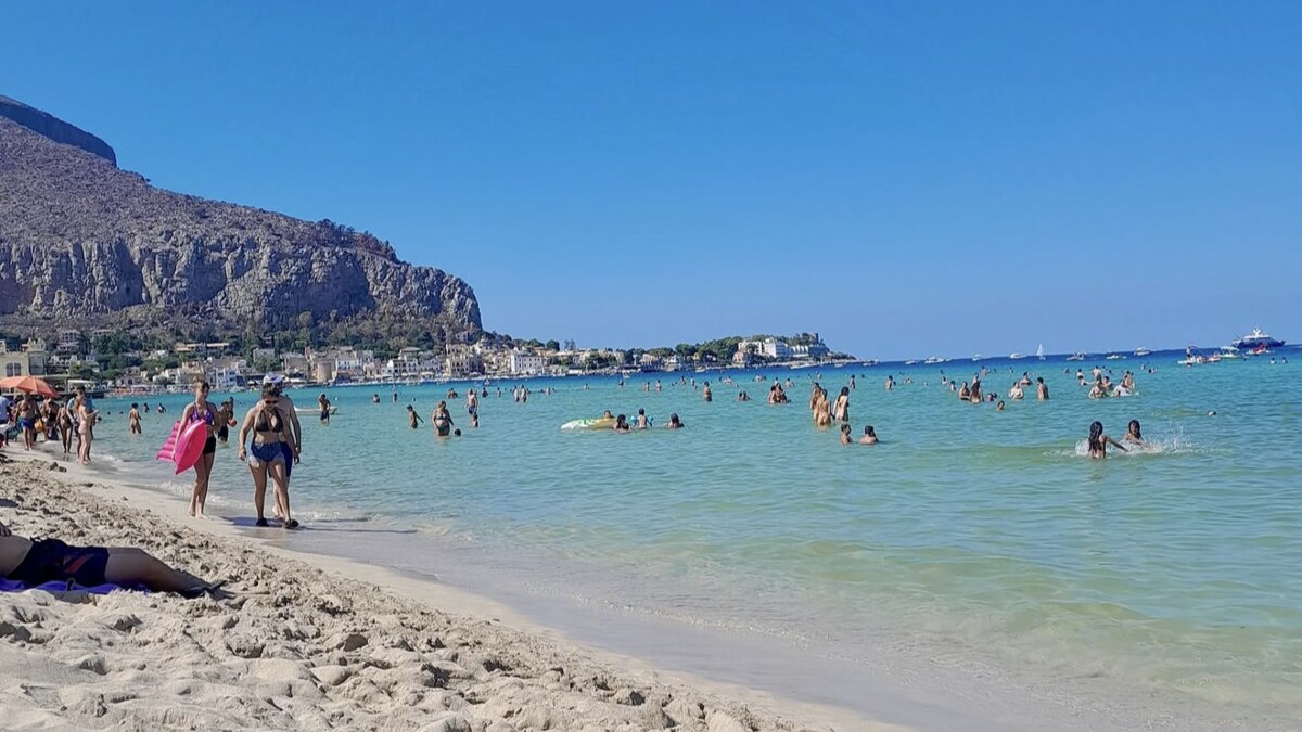 Mondello beach near Palermo, white sand and shallow turquoise water busy with swimmers, below a rocky headland with the town beyond