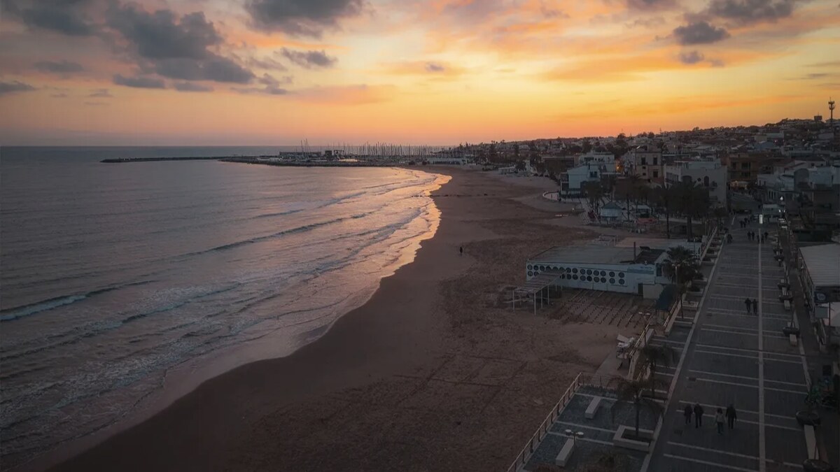 Marina di Ragusa in south-east Sicily at sunset, a long sandy resort beach with a promenade and lidos stretching toward the town under a golden sky