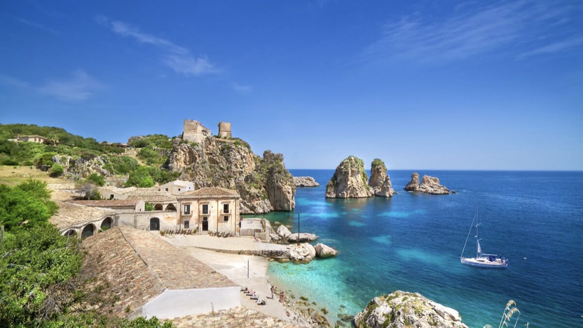 Tonnara di Scopello in western Sicily, weathered sea stacks rising from clear water beside the old tuna fishery buildings
