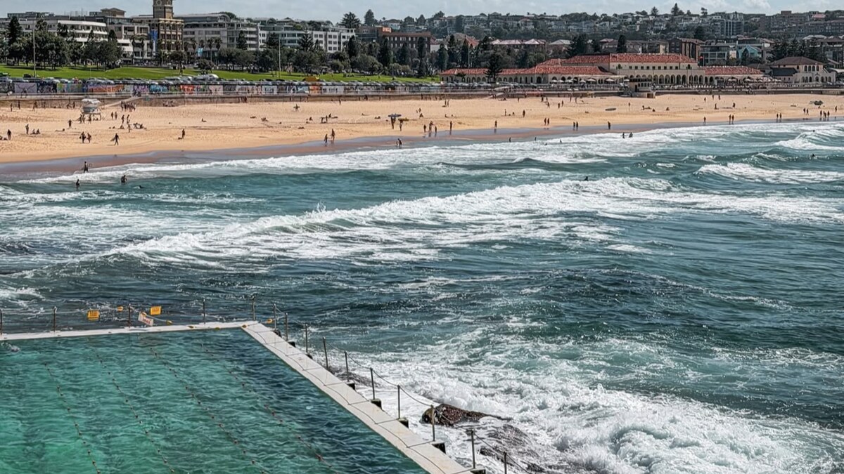 The Bondi Icebergs ocean pool on the rocks at the southern end of Bondi Beach in Sydney, with surf breaking alongside and the golden beach and suburb stretching behind