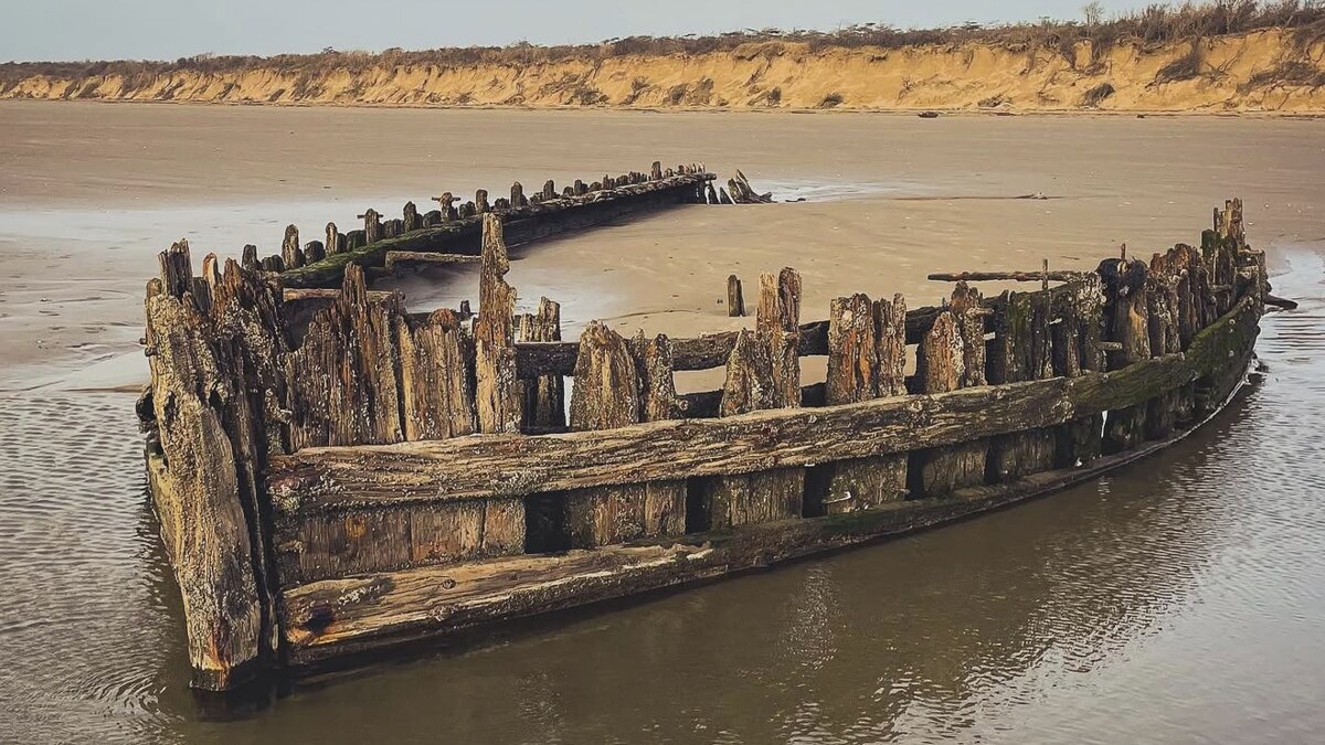 Cefn Sidan beach at Pembrey in Carmarthenshire, the weathered timbers of an old shipwreck emerging from the vast flat sand below the dunes