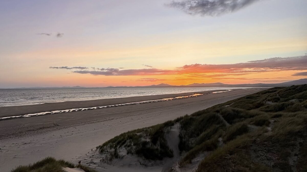 Harlech Beach in North Wales at sunset, marram dunes above the flat sand with the sea and a pink-and-orange sky