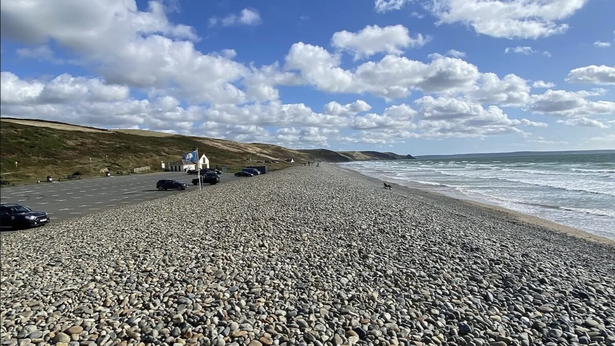 Newgale beach in Pembrokeshire, the steep pebble storm bank and roadside car park above the sand, with surf rolling in under a big cloud-streaked sky