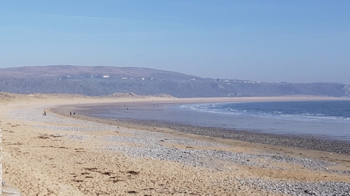 Oxwich Bay on the Gower, a long curve of sand and a pebble bank sweeping toward a headland, with hills behind under a clear sky