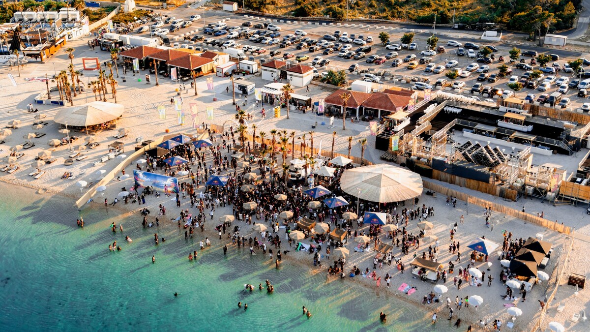 An aerial view of Zrce beach near Novalja on Pag, the pebble party beach lined with open-air clubs and umbrellas above clear turquoise water