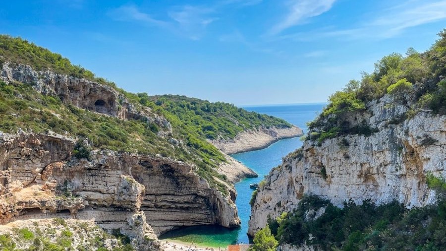 Stiniva cove on Vis, a pebble beach at the foot of two tall cliff walls that almost meet, opening through a narrow gap to the open sea